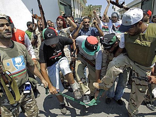 Rebellenkämpfer zerreißen eine grüne Flagge, das Symbol für die Ära Gaddafi. Rebellenkämpfer zerreißen eine grüne Flagge, das Symbol für die Ära Gaddafi.