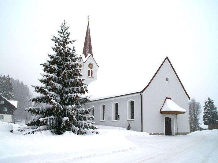 Ein Weihnachtsbaum mit vielen Tannenzapfen vor der tief verschneiten Pfarrkirche von Sibrtagsgfäll
