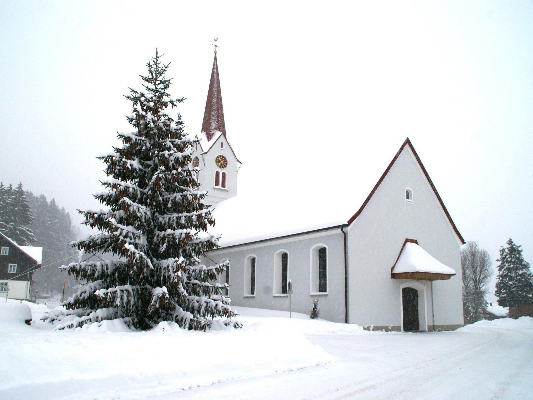 Ein Christbaum mit vielen Tannenzapfen vor der tief verschneiten Pfarrkirche in Sibratsgfäll lässt Weihnachtsstimmung aufkommen.