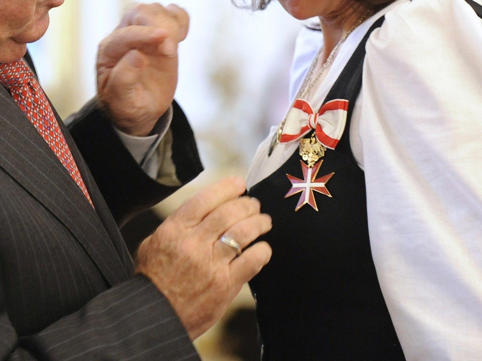 Das Goldene Ehrenzeichen besteht aus einem Komturkreuz und einem Flechtbandornament an einem rot-weißen Halsband.