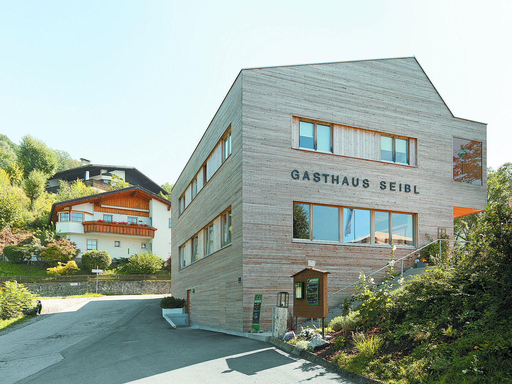 Giebelständig zum Hang wie die Nachbarschaft – ohne Lederhosenarchitektur. Mit markantem asymmetrischem Dach wegen des gemeinsamen Giebels und der angehängten Loggia. Giebelständig zum Hang wie die Nachbarschaft – ohne Lederhosenarchitektur. Mit markantem asymmetrischem Dach wegen des gemeinsamen Giebels und der angehängten Loggia.