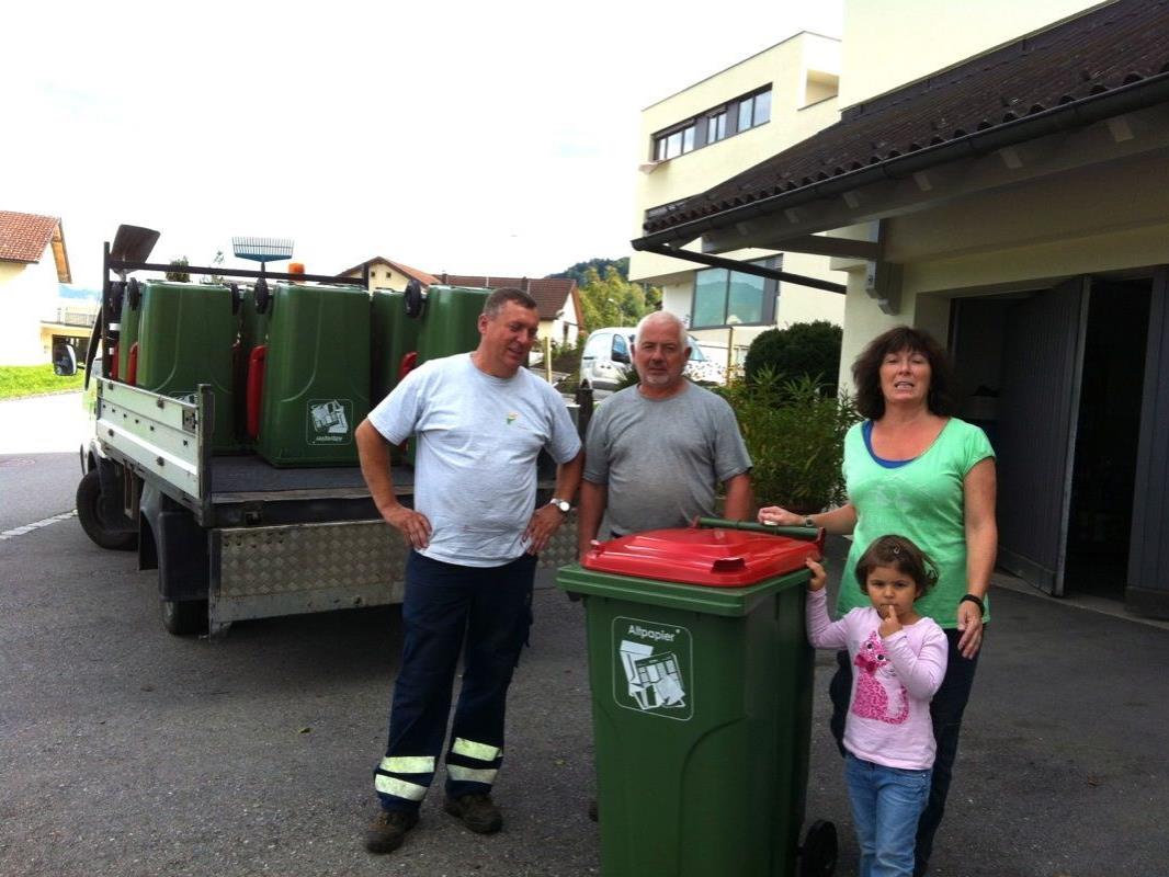 Die Gemeindearbeiter Aladin und Helmut liefern die Kunststofftonne mit 240 Litern Volumen bei Familie Rita Morscher und Mia ab