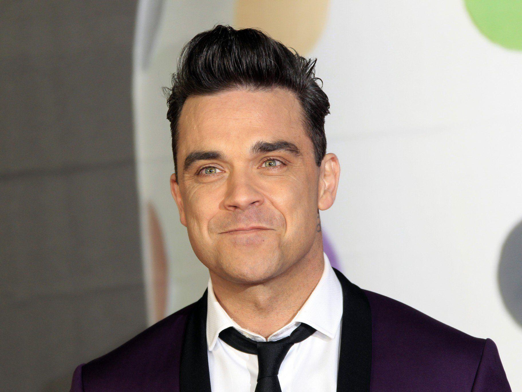 Robbie Williams signiert während eines Konzert den Hintern eines Fans.