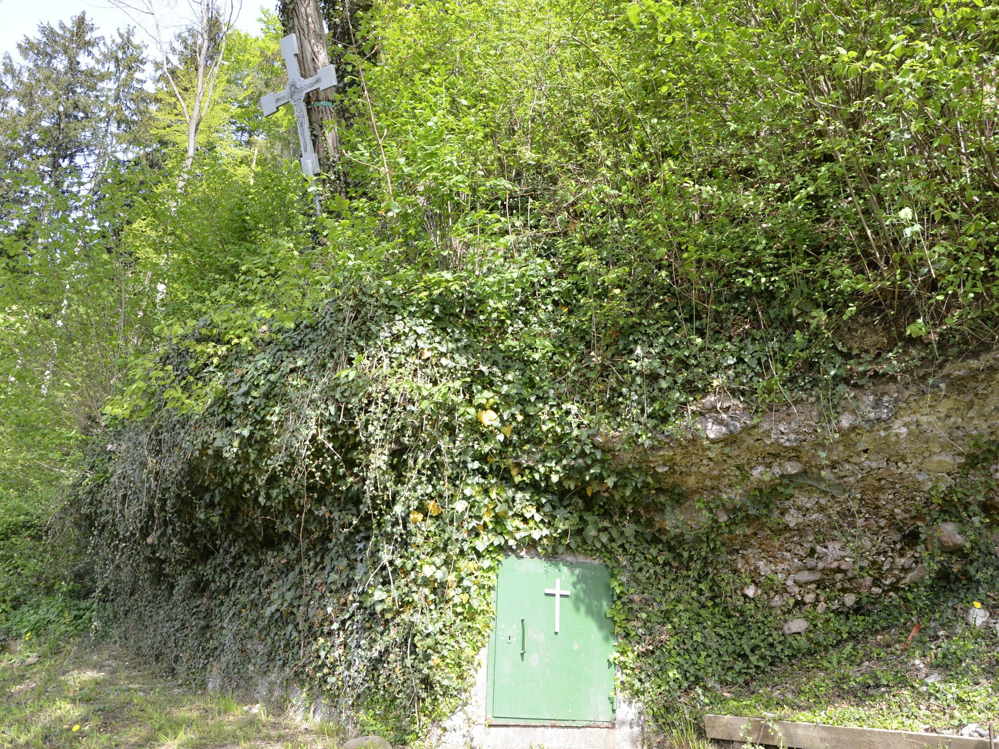 Das silberne Kreuz und der Eingang zur Kreuzquelle beim Feuerwehrhaus in Muntlix.