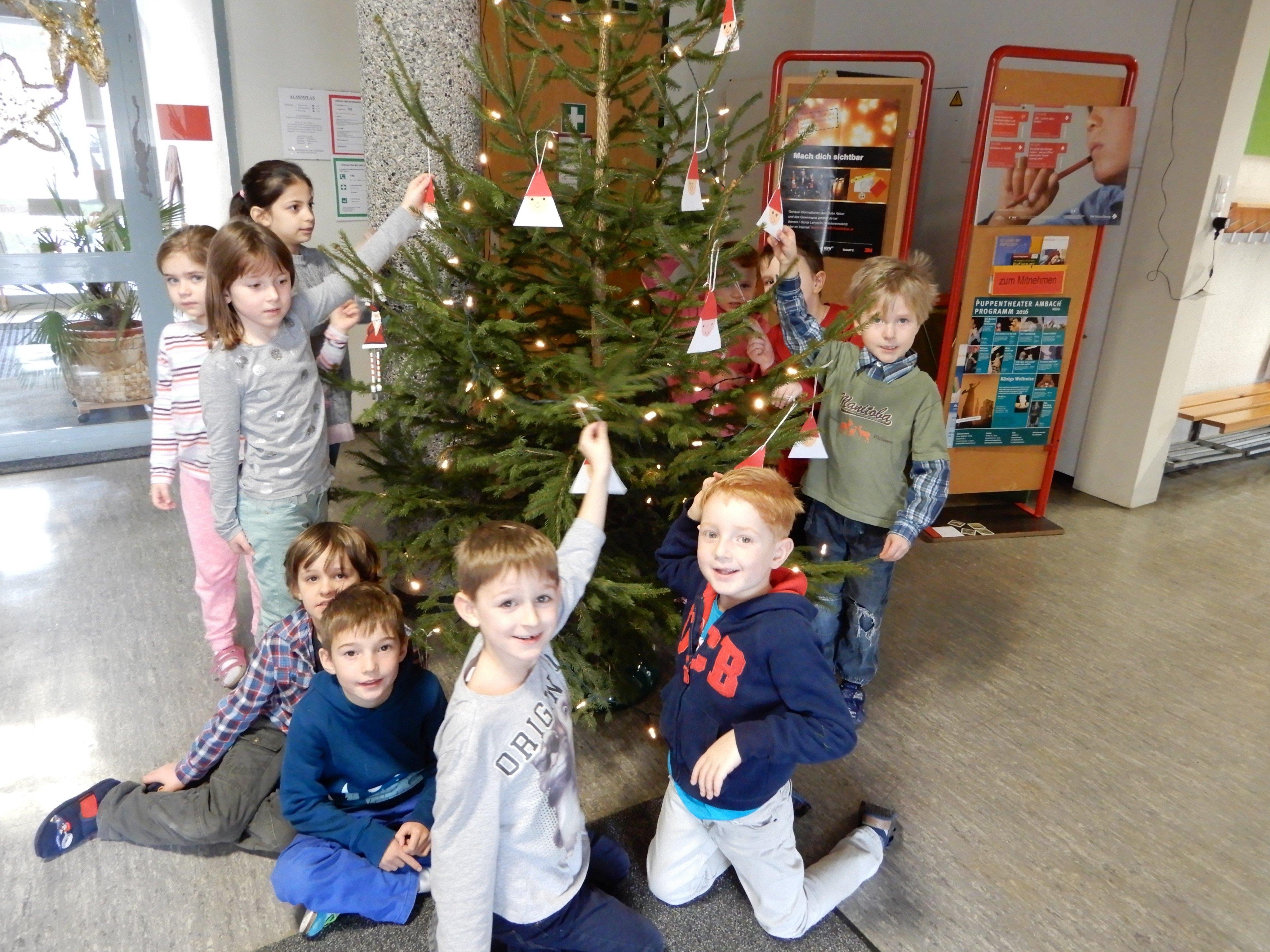 Die Kinder der 1 a VS Leopold schmücken ihren Weihnachtsbaum im Schulgang mit ihren neuen Anhängern noch fertig.